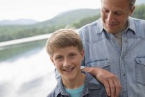 Father leaning on son shoulder outdoors on lake shore. — Stock Photo