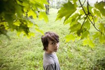 Pre-adolescent boy looking up behind tree foliage in woods. — Stock Photo