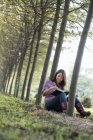 Mulher sentada e lendo livro sob árvores na floresta
. — Fotografia de Stock