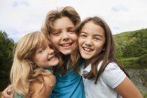 Three girls posing side by side in front of forest lake. — Stock Photo