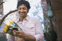 Junger Mann hält Strauß gelber Rosen in der Hand und benutzt Smartphone. — Stockfoto