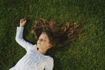 Elementary age girl resting on green grass with eyes closed — Stock Photo
