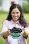 Hispanic woman with curly hair holding bowl of freshly picked blackberries in country garden. — Stock Photo