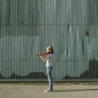 Pre-adolescent girl playing the violin on street against corrugated metal wall — Stock Photo