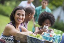 Jeune femme souriant à la caméra avec des amis à la table de pique-nique dans le jardin de campagne . — Photo de stock