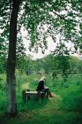 Женщина сидит на деревянном сиденье в зеленой сельской местности
. — стоковое фото