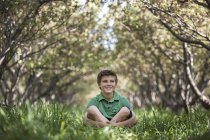 Boy sitting with crossed legs in woodland tunnel of overarching tree branches. — Stock Photo