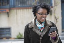 Жінка в окулярах посміхається і використовує смартфон на вулиці . — стокове фото