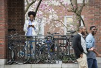 Mulher mensagens de texto em rack com bicicletas trancadas com dois homens andando na rua . — Fotografia de Stock