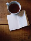Чашка кофе и рукописный журнал на деревянном столе . — стоковое фото