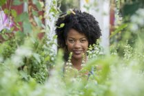 Porträt einer afrikanisch-amerikanischen Frau in einer Gärtnerei, umgeben von grünem Laub. — Stockfoto