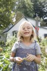 Blonde girl in pinafore dress holding green beans in country. — Stock Photo