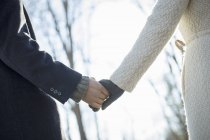 Vista recortada de pareja cogida de la mano en el bosque en invierno . - foto de stock