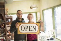Couple standing in antique store and holding large OPEN sign. — Stock Photo