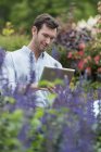 Hombre adulto medio usando tableta digital en vivero de plantas orgánicas . - foto de stock