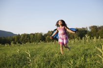 Ragazza pre-adolescente che corre attraverso il campo indossando ali di tessuto farfalla . — Foto stock