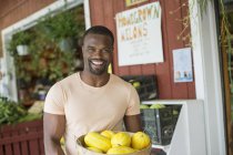Hombre alegre llevando cesta de calabaza amarilla verduras en el mercado agrícola ecológico . - foto de stock
