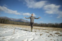 Homem de malha jumper e botas de lama de pé com os braços estendidos na paisagem rural nevada . — Fotografia de Stock