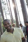 Homme adulte moyen souriant et regardant à la caméra avec des amis rassemblés dans des pins au bord du lac . — Photo de stock