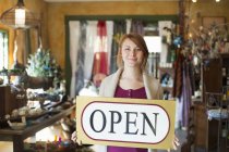 Femme debout dans un magasin d'antiquités et tenant le signe OUVERT . — Photo de stock