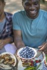 Jeune homme tenant un bol de bleuets frais à la table de pique-nique en famille dans les bois . — Photo de stock