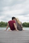 Homme et femme assis ensemble sur une jetée près d'un lac . — Photo de stock