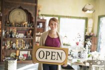 Woman standing in antique store and holding door sign. — Stock Photo