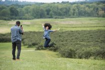 Uomo scattare foto di donna che salta con le braccia tese in campagna . — Foto stock