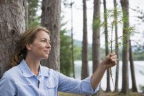 Mature woman holding twig on shore of lake in countryside. — Stock Photo
