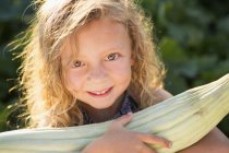 Elementary age girl with curly hair holding corn on the cob in garden. — Stock Photo