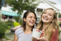 Chicas adolescentes abrazando, riendo y sosteniendo tazón de helado - foto de stock