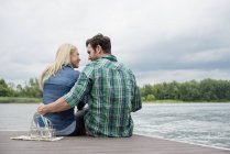 Mann und Frau sitzen Kopf an Kopf und umarmen sich auf Steg mit Brille am See. — Stockfoto
