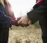 Cropped view of couple in winter coats holding hands in wintry forest. — Stock Photo