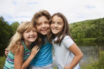Tre ragazze in posa fianco a fianco di fronte al lago foresta . — Foto stock