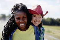 Female friends smiling and embracing in field with irrigation sprinklers. — Stock Photo