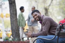 Young man sitting on city bench with people talking in background. — Stock Photo