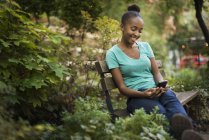 Adolescente assise sur un banc dans un parc et utilisant un smartphone . — Photo de stock