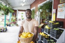 Fröhlicher Mann trägt Korb mit gelbem Kürbisgemüse auf Bio-Bauernmarkt. — Stockfoto