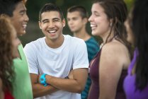 Teenage boy standing with arms crossed in group of young laughing friends outdoors. — Stock Photo