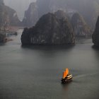 Barco chino con velas de naranja en el agua de mar entre las rocas en la bahía de Halong, Vietnam, Asia - foto de stock