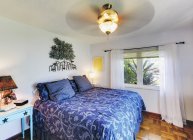 Bett mit filigranem Design, blauem Bettzeug, drehbarem Deckenventilator und Fenster — Stockfoto