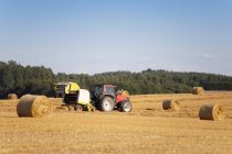 Feno de colheita de tractores e fardos de feno de embalagem no terreno, Estónia — Fotografia de Stock
