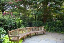 Длинная округлая скамейка в зеленых кустах с цветами — стоковое фото