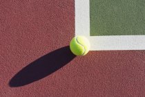Крупный план теннисного мяча на краю теннисного корта при солнечном свете — стоковое фото