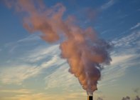 Steam from smokestack colored by sunset against cloudy sky — Stock Photo