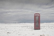 Telephone booth in snowy landscape under storm — Stock Photo