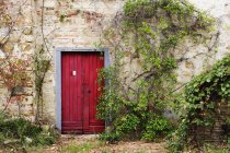 Puerta roja en antigua casa de campo de ladrillo y piedra en Siena, Italia, Europa - foto de stock