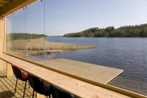 Bâtiment rustique au bord du lac et quai en bois par la fenêtre — Photo de stock