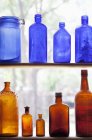Antique bottles stacked in rows on shelves by window — Stock Photo