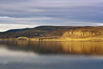 Barren cliffs reflecting in sunlight in water with metal bridge, Columbia River, Vantage, Washington, USA — Stock Photo